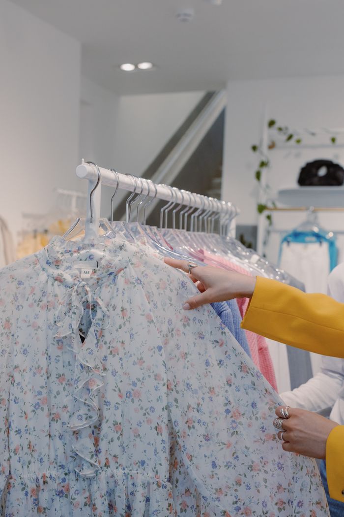 Mastering the First Impression: Your intriguing post title goes here Woman browsing floral print dresses on a clothing rack indoors in a fashion store.